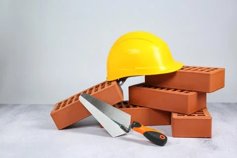 Red bricks, trowel and hardhat on textured table against light background 스톡 사진
