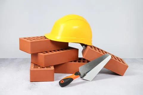 Red bricks, trowel and hardhat on textured table against light background Stock Photos