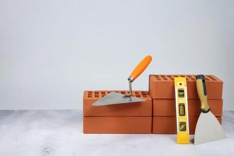 Red bricks, trowels and building level on textured table against light back.. Stock Photos
