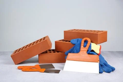 Red bricks, trowels and gloves on textured table against light background Stock Photos