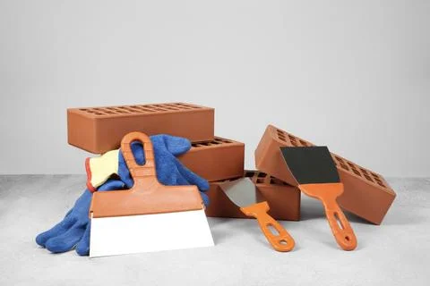 Red bricks, trowels and gloves on textured table against light background Stockfoto's