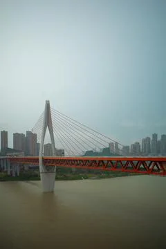 Red bridge spans wide river under cloudy sky Stock Photos