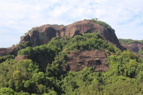 Red-brown rock cliffs rising above dense green forest Stock-Fotos