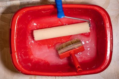A red bucket of glue containing a roller and brush to cover the wall Stock Photos