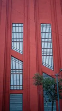 Red Building With Long Vertical Windows Righ Behind a Tree Stock Photos