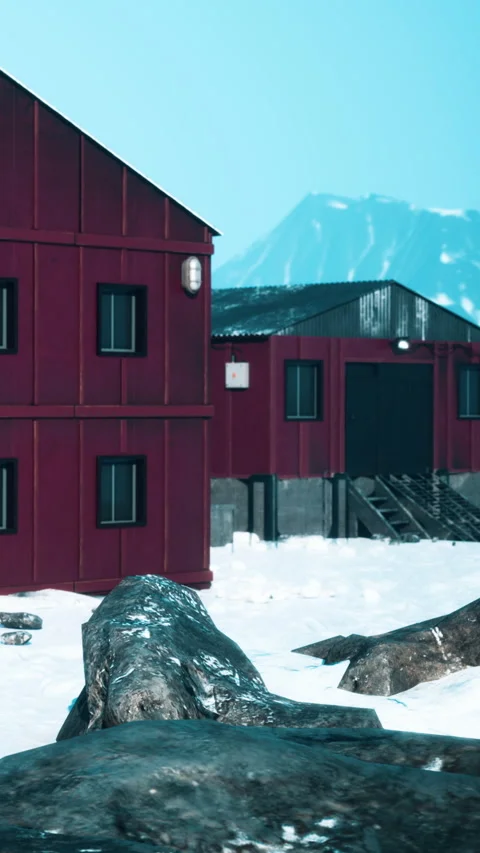 Red buildings stand on snow with mountains in background during day Stock Footage 346758629