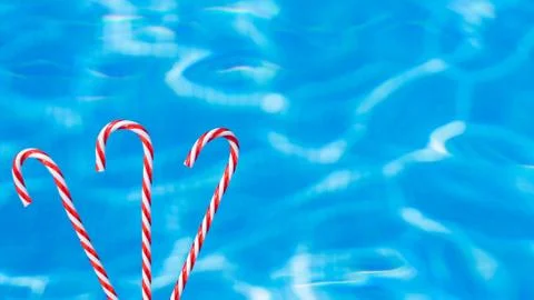 Red candy cane on blue water background. New Year and Christmas on pool. Chri Stock Photos