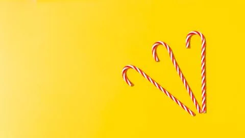 Red candy cane on yellow background. New Year and Christmas on beach on sea.  Stock Photos
