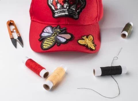 Red cap with various patches, threads, scissors and a neele on white background Stock Photos