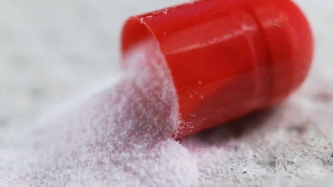The red capsule lies open on a gray background. A fine white powder spilled out Stock Footage