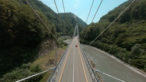 Red car drives along cable-stayed bridge over mountain river Stock Footage 141668228