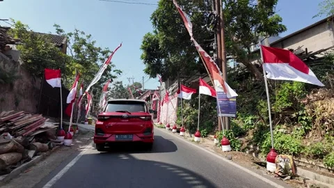 Red car drives through festive street lined with flags Stock Footage 345156658