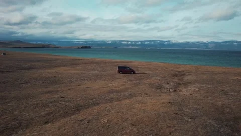 A red car is driving slowly along a dirt road on the shore of Lake Baikal Stock Footage 321907832