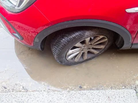 Red car experiencing a flat tire, creating a frustrating street breakdown s.. 스톡 사진
