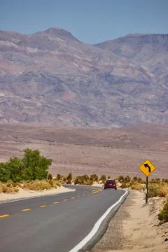 Red car making sharp turn on paved road in desert leading to mountains 스톡 사진