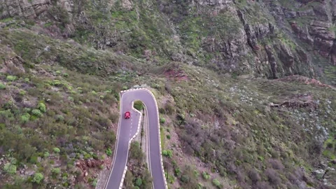 Red car navigates winding mountain road with sharp turns and lush greenery. Auto Видео 341125727