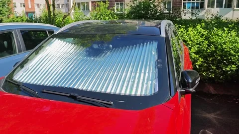 Red car parked outdoors with a reflective sunshade installed on the windshield Stock Footage 338168460