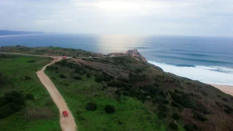 Red car riding on bumpy road in grassy field, Nazare coastline Stock Footage 156633848