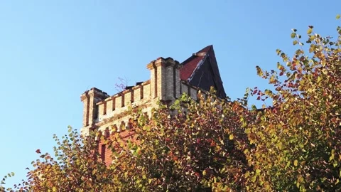 Red castle tower from behind trees with colorful leaves, blue sky Vidéo 163679221