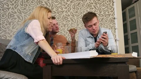 Red cat under the table, eating crumbs, while young friends eating pizza and Stock-Footage 73482423