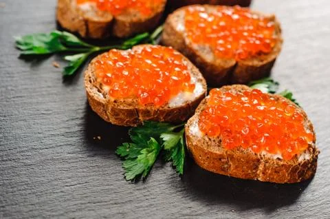 Red caviar on bread on slate background. 库存照片