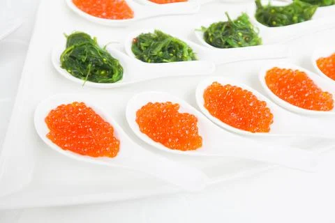 Red caviar close-up in white spoons on banquet 库存照片
