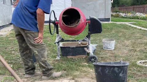 Red cement mixer operating on grass with man watching Stock Footage 316539418