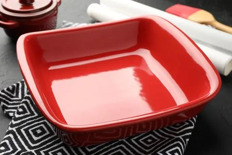 Red ceramic casseroles, baking parchment paper and brush on black table, cl.. Stockfoto's
