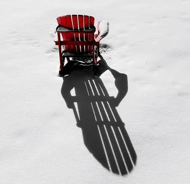 Red chair casting a long shadow on snow in a winter landscape Stock Photos