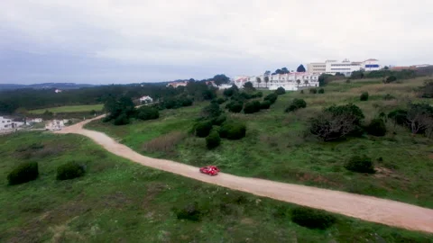 Red Chargers car riding on bumpy road next to grassy field in Nazare Stock Footage 156633774