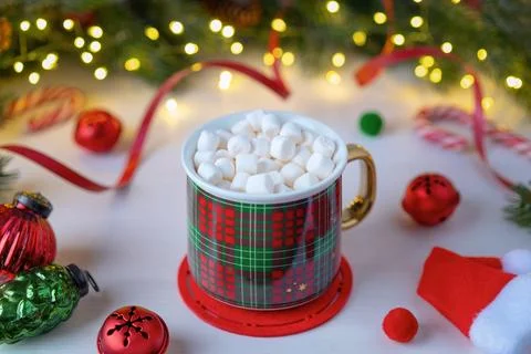 A red checkered mug with marshmallows on a background of Christmas decorations. Stock Photos