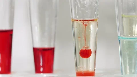 Red chemical drop sinking in clear liquid within test tube for scientific e.. Stock Footage 334605312