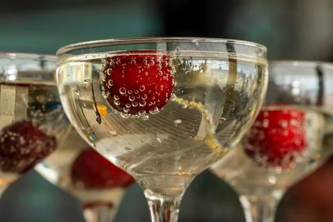 Red cherries in air bubbles float in champagne glasses. Stock Photos