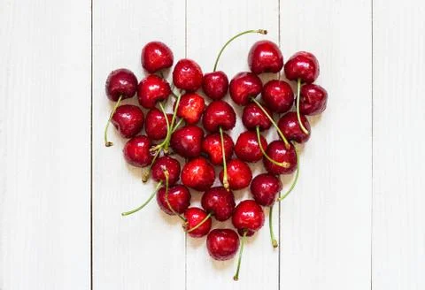 Red cherries in heart shape on white wooden background Stock Photos
