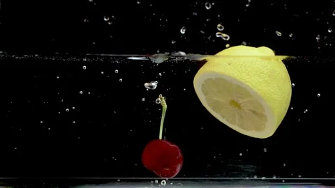 Red cherry falls next to lemon floating in water tank, slow motion Stock Footage 111945811