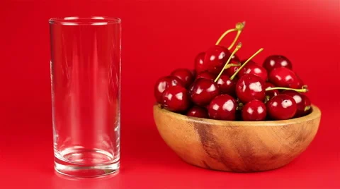Red cherry juice being poured in a glass and red ripe cherries in wooden bowl on Stock Footage 63982351