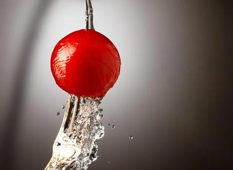 Red cherry tomato on a silver fork. A jet of water, splashes of water. Black Stock Photos