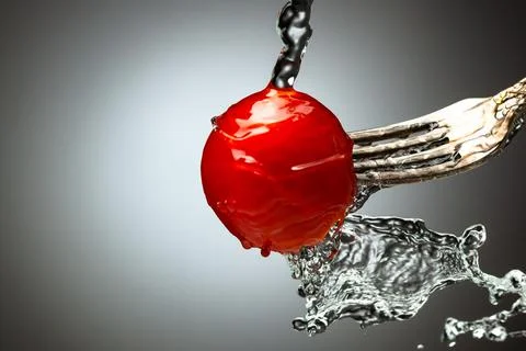 Red cherry tomato on a silver fork. A jet of water, splashes of water. Black Stock Photos