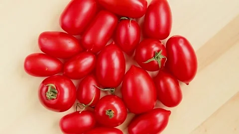 Red cherry tomatoes plum shape rotating on wooden serving table Video stock 157776509