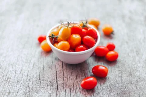 Red cherry tomatoes in white ceramic bowl on old wooden background, vintage t Stock Photos