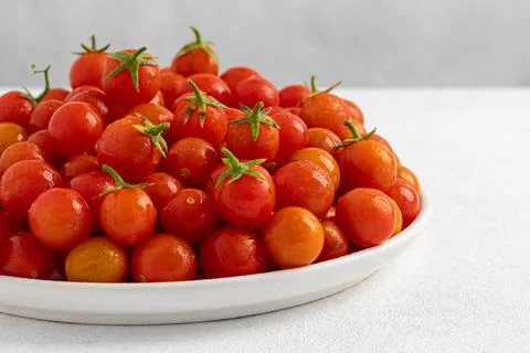 Red cherry tomatoes in a white dish on a light, minimalism Stock Photos