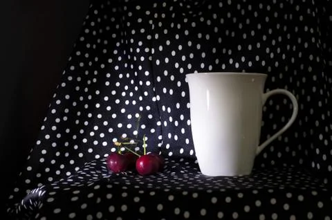 Red cherry with white ceramic mug for hot drink on polka white dot on black f Stock Photos