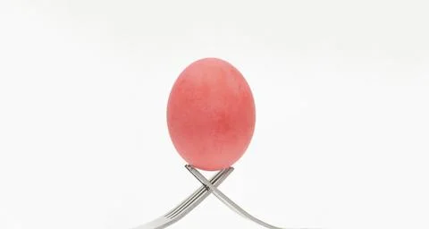 A red chicken egg is placed on the tip of a cutlery on a white background. Stock Photos