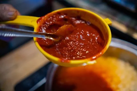 Red chili pepper paste in plastic strainer above cooking pot Stock Photos