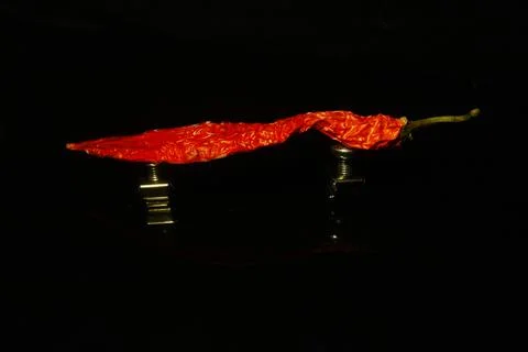 Red chilli on a metallic support  isolated on black with reflection Foto stock