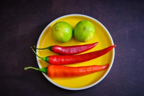 Red chilli pepper and lemon on yellow plate in dark background Stock Photos