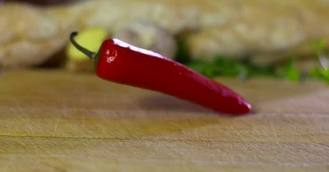 Red Chilli pepper falls onto chopping block recipe ingredient Video stock 77530526