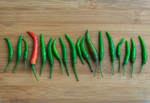 A red chilli pepper in Green chilli pepper on chopping block Stock Photos