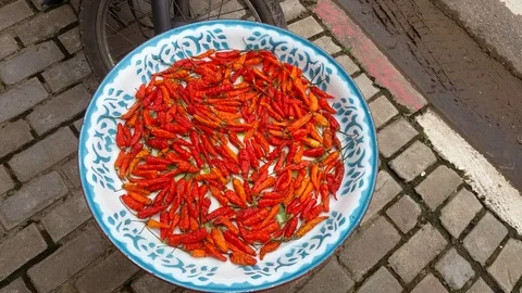 Red chillies drying on plate on sidewalk, next to motorcycle wheel Видео 74987203