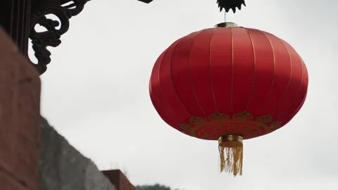 Red Chinese lantern hanging under eave, cloudy sky backdrop, ornate wooden Stock Footage 335163959
